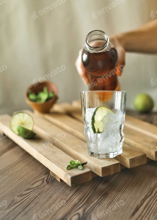 Preview: A hand holds a bottle with tea to fill the glass with ice. Making ice tea with lime and mint.