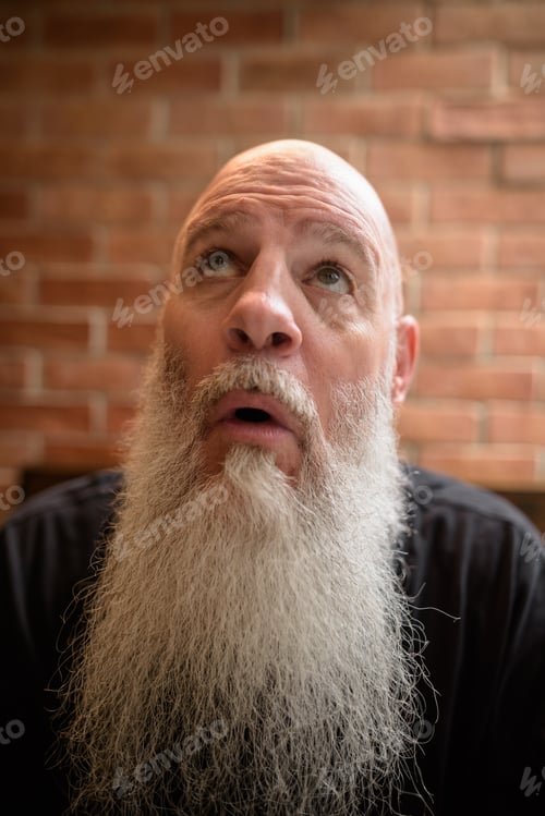 Preview: Portrait of mature man feeling surprised and scared while looking up with long gray beard