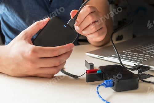 Preview: Male hand connecting the hard drive with a USB cable to a laptop computer and USB splitter device