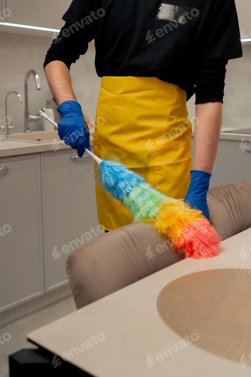 Preview: close up in the apartment cleaner in a yellow apron is cleaning chairs with a dust brush
