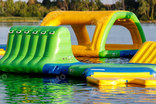 Preview: Inflatable kids water amusement park floats on lake pond surface on sunny day.