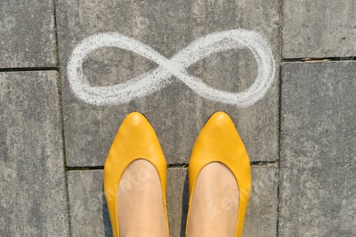 Preview: Infinity sign on gray sidewalk with woman legs, top view