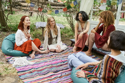 Preview: happy multiethnic girlfriends talking on colorful blanket in park, women retreat concept