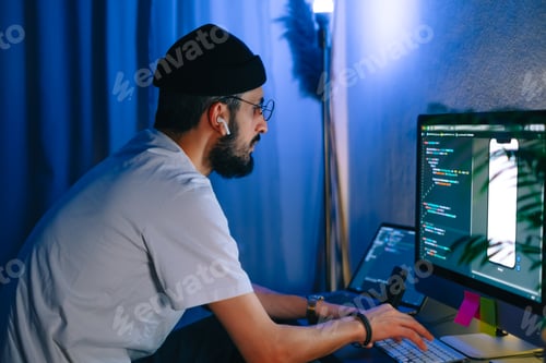 Preview: Young man mobile developer writes program code on a computer, programmer work in home office.