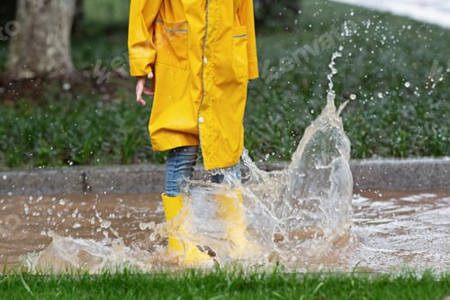 Preview: Happy little girl in yellow rain jacket jumping on puddles outdoor at summer day