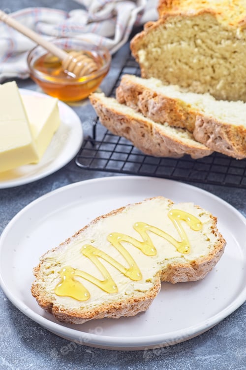 Preview: Freshly baked white Irish soda bread with butter and honey served on a plate, vertical