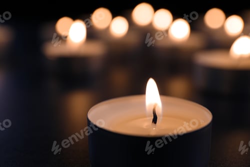 Preview: Burning candle on table in darkness, closeup. Funeral symbol