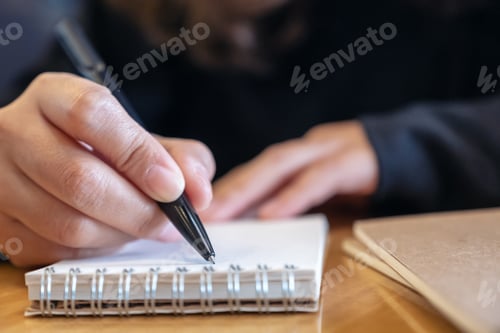 Preview: Closeup image of a woman writing on blank notebook on wooden table