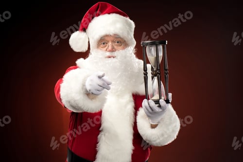Preview: Santa Claus with hourglass and pointing at camera
