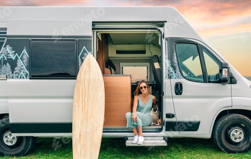 Preview: Woman sitting with her dog at the door of her camper van during a trip