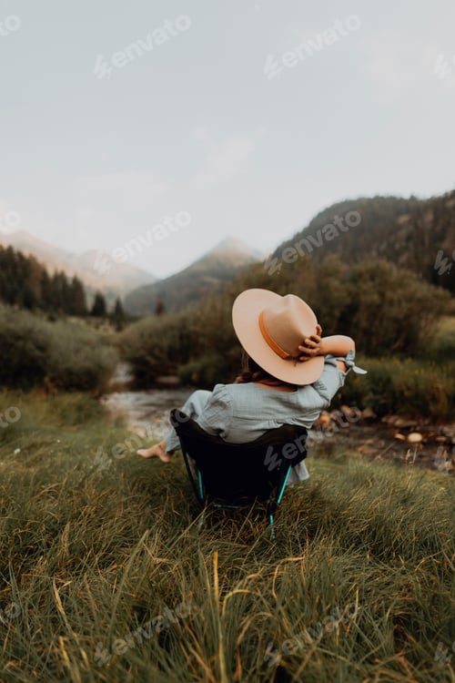 Preview: Young woman relaxing in deckchair by rural river, rear view, Mineral King, California, USA