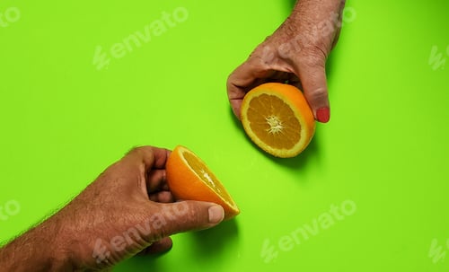 Preview: A couple trying to put their orange back together again using hands in frame on a green background