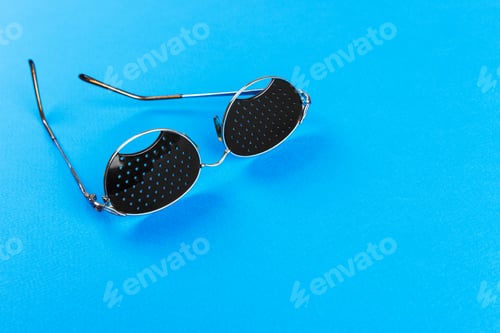 Preview: Black pinhole glasses on blue background. Medical concept. Top view