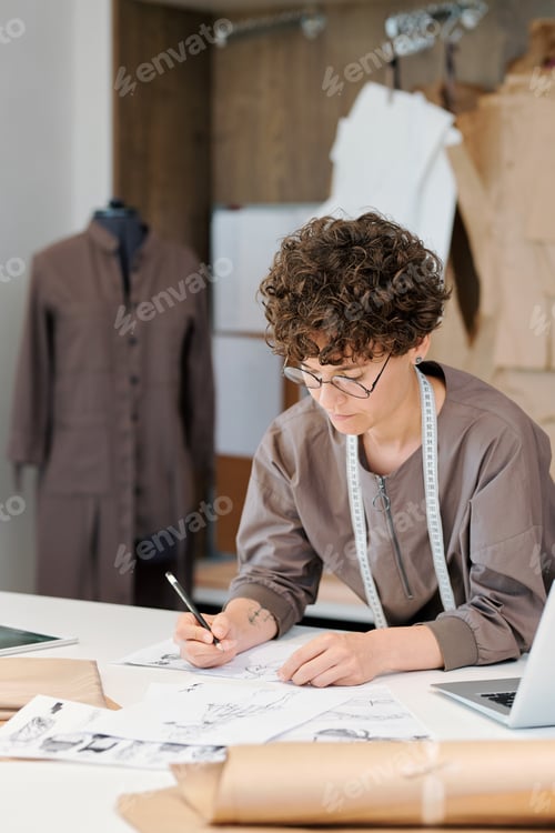Preview: Young brunette female bending over desk while making fashion sketches