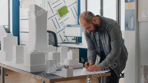 Preview: Man engineer analyzing building model to design blueprints plans on table