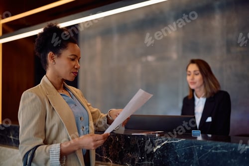 Preview: African American woman checking in at reception desk in a hotel.