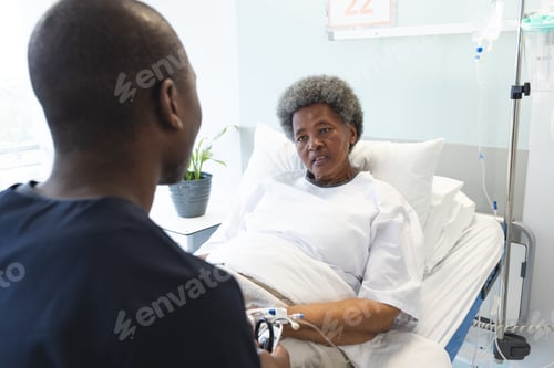 Preview: African american male doctor talking with senior female patient in hospital room