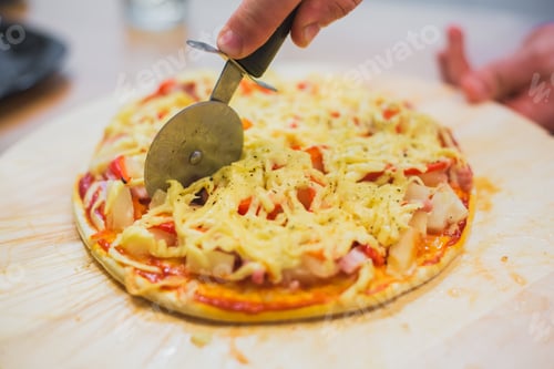Preview: Cutting pizza with pizza cutter on striped bamboo cutting board.
