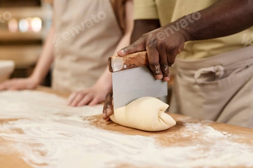 Preview: Close up of Black man cutting dough for fresh bread in bakery