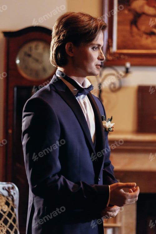 Preview: Stylish groom in bow tie and blue suit getting ready in the morning in hotel