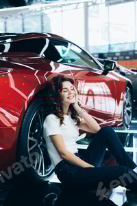 Preview: selective focus of happy woman with closed eyes sitting on floor near new red car