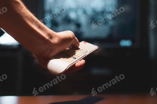 Preview: hands in the dark hold a tv remote and switch channels d
