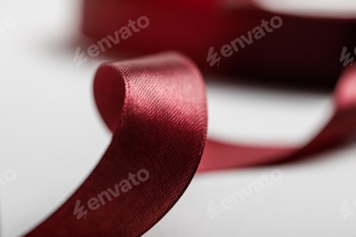 Preview: selective focus of shiny silk curved burgundy ribbon on grey background