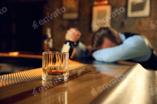 Preview: Drunk man sleeping at bar counter with focus on alcoholic drink in glass