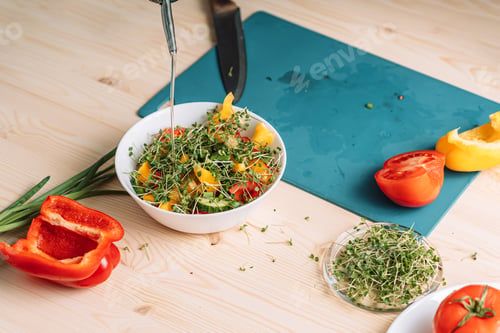 Preview: Lady pouring oil on vegetable salad with microgreens