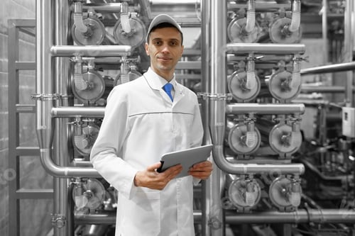 Preview: Portrait of man in a white robe and a cap standing in production department of dairy factory with