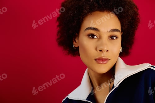 Preview: A young emotional woman with curly hair poses against a vibrant red background in a creative studio