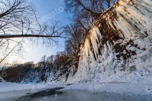 Vista previa: Amanecer en el río congelado. Hielo, nieve y grandes carámbanos en un acantilado