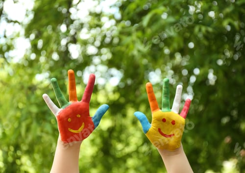 Preview: Kid with smiling faces drawn on palms in green park, closeup