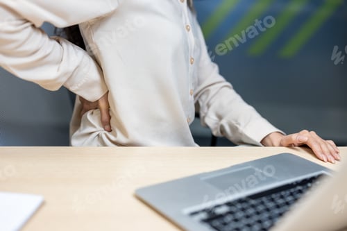 Preview: Office worker experiences back pain while sitting at desk with laptop and presses on lower back for