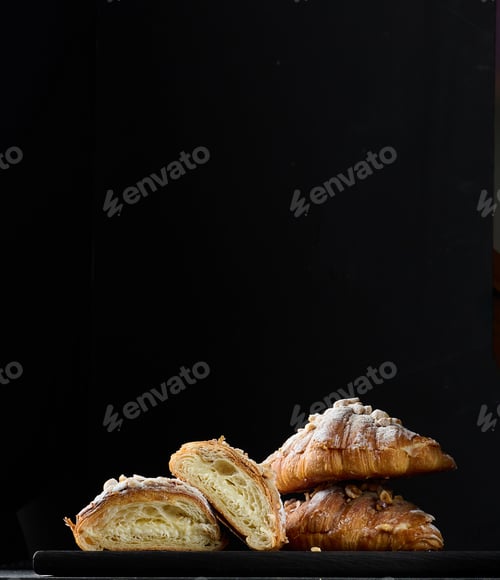 Preview: Stack of baked croissants sprinkled with powdered sugar on a black background
