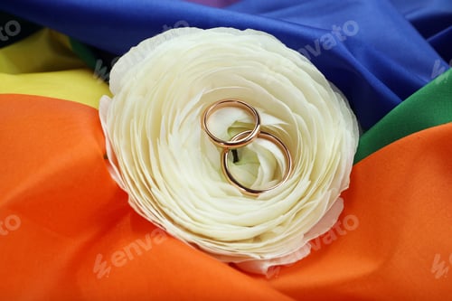 Preview: Wedding rings and flower on rainbow LGBT flag, closeup