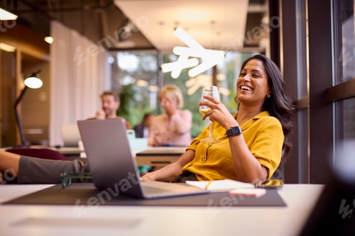 Preview: Mature Businesswoman With Feet On Desk In Office Drinking Wine