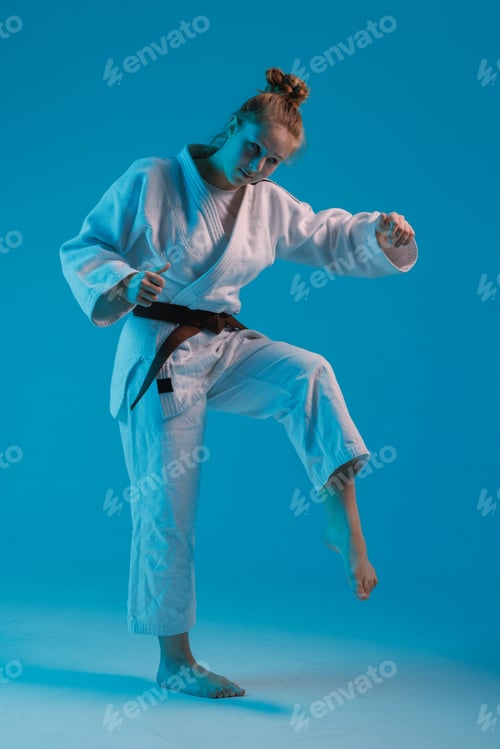 Preview: girl judoka in a white kimano with a black belt on a blue background, studio photo