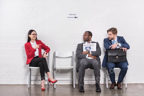 Preview: smiling asian businesswoman pointing at multiethnic businessmen while waiting for job interview