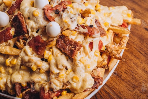 Preview: Closeup shot of a dish with french fries, sausages topped with cheese and corn on a wooden table.