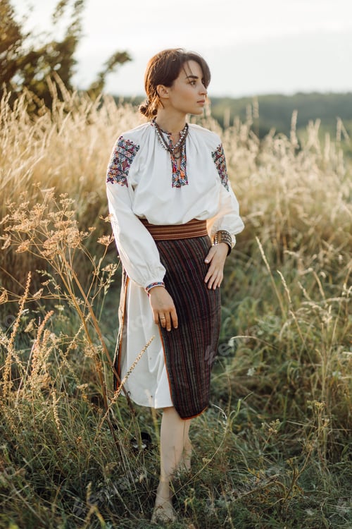 Preview: Young woman in traditional national embroidered shirt and skirt on nature at sunset.