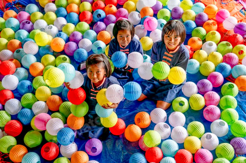 Preview: Group of three Asian girls sit among many paper lamps with multicolor and they look happy