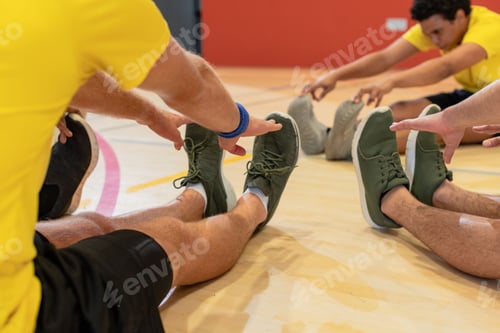 Preview: Diverse male teammates in yellow shirts, black shorts stretching on court floor touching shoes