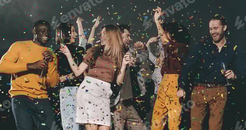 Visualização: Grupo de jovens alegres dançando e jogando confetes enquanto desfrutam de uma festa na boate