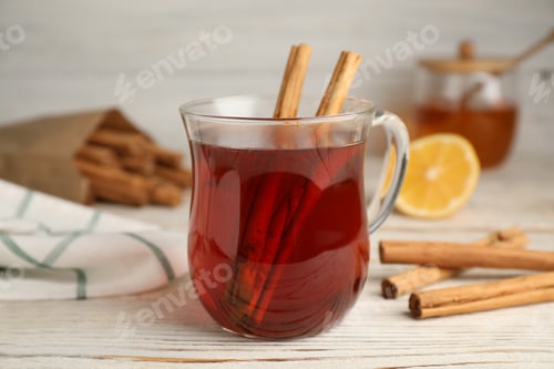 Preview: Glass cup of hot tea with aromatic cinnamon on white wooden table, closeup