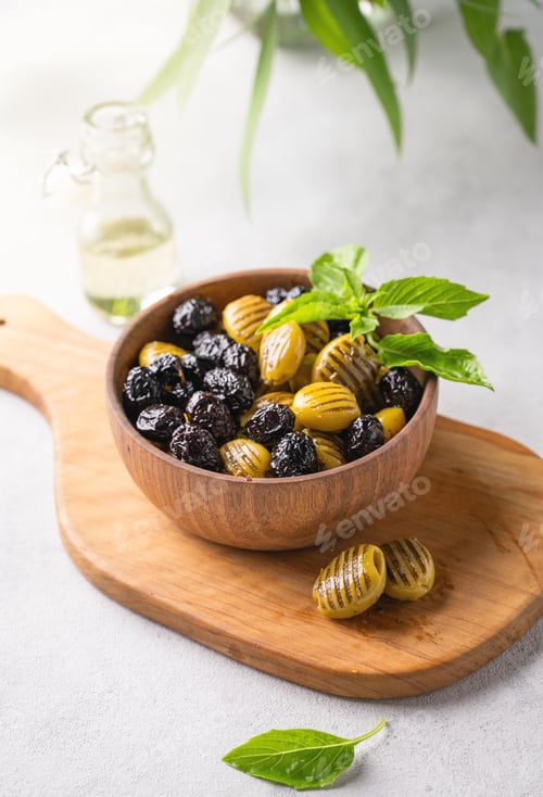 Preview: A set of green and black dried olives in wooden bowl on a light background with olive oil and basil
