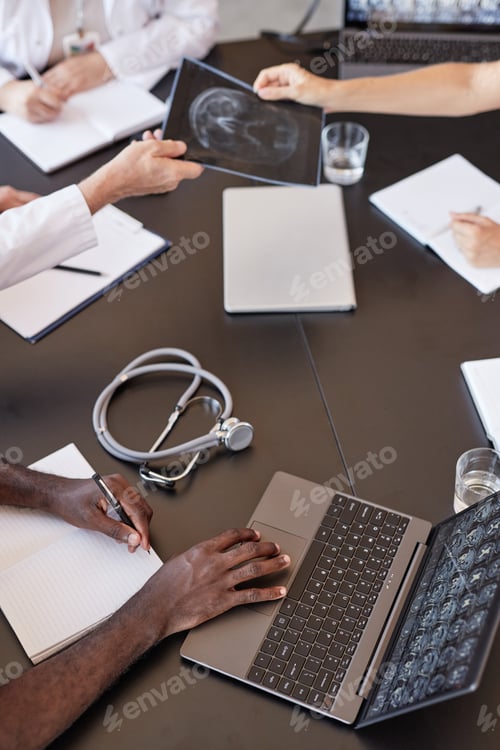 Preview: Doctor Using Laptop Checking X Ray Scan Results at Meeting Table with Colleagues Indoors