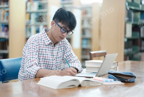 Preview: Young Asian male sitting inside a library alone doing research.