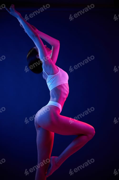 Preview: Standing with hands up. Young woman in underwear is in the studio with neon lights
