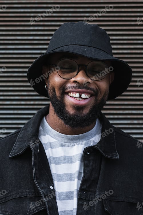 Preview: Smiling black hipster man in hat looking at camera